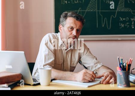 Teacher sitting in the classroom holding  a pen and looking at the camera Back to school Stock Photo