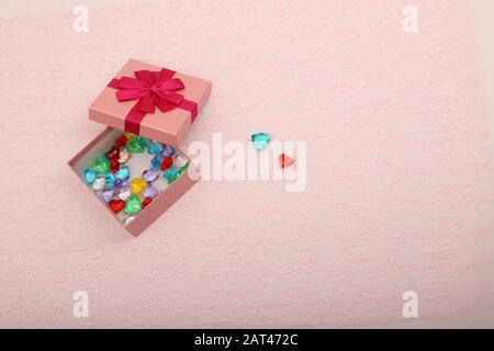 Gift in a pink box on a light background with a copy space. Opened gift box for a girl with coloured hearts inside. Two hearts and opened gift box in Stock Photo
