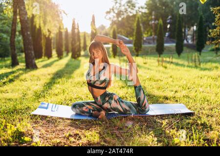 Girl doing yoga  sitting  in pigeon pose outdoors . Stock Photo