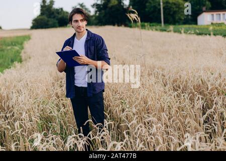 Ful-length portrait of agronomist standing in a wheat field taking control of the yield and dreamly looking Stock Photo
