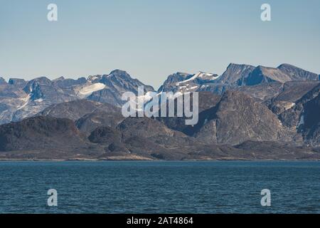 Arctic landscape of Greenland on a sunny day in Summer. Beautiful view of mountains with Snowy peaks and Glaciers along the Atlantic Ocean. Stock Photo