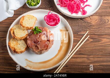 Salt marinated silver carp, diced, next to onion marinated in wine vinegar, fried croutons. Decorated with microgreen. On a wooden background. Copy sp Stock Photo