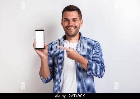 Smiling man holding a smartphone and pointing to screen - Mockup image of white empty blank screen of phone Stock Photo