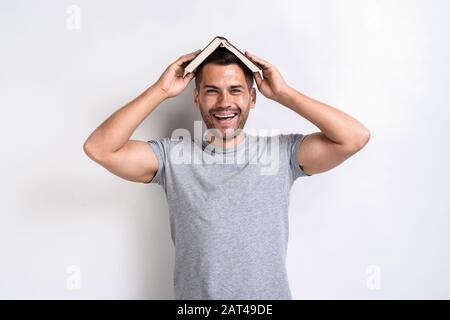 Funny man put the book on his head and happily looking at the camera.- Image Stock Photo