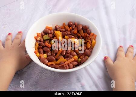 boiled red kidney beans with parsley in white bowl closeup on the table. Kids hands Stock Photo