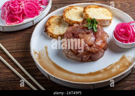 Salt marinated silver carp, diced, next to onion marinated in wine vinegar, fried croutons. Decorated with microgreen. On a wooden background. Copy sp Stock Photo
