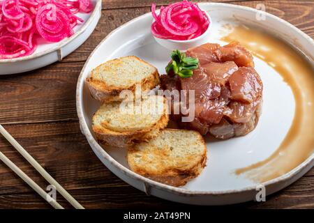 Salt marinated silver carp, diced, next to onion marinated in wine vinegar, fried croutons. Decorated with microgreen. On a wooden background. Copy sp Stock Photo