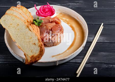 Salt marinated silver carp, diced, next to onion marinated in wine vinegar, fried croutons. Decorated with microgreen. On a wooden background. Copy sp Stock Photo