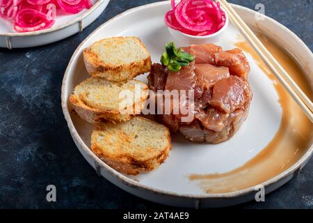 Salt marinated silver carp, diced, next to onion marinated in wine vinegar, fried croutons. Decorated with microgreen. On a wooden background. Copy sp Stock Photo