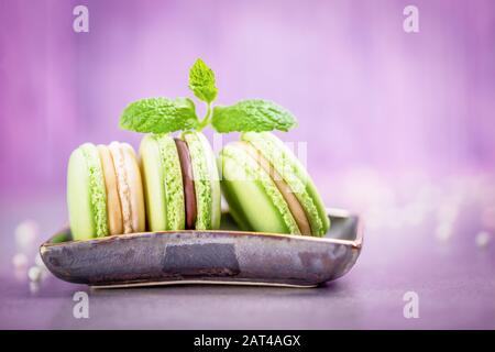 Delicious french macaroons or macarons. Mint cookies with chocolate and vanilla cream on a pale pink violet background, copy space Stock Photo