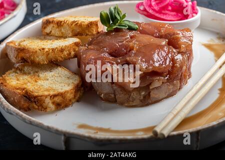 Salt marinated silver carp, diced, next to onion marinated in wine vinegar, fried croutons. Decorated with microgreen. On a wooden background. Copy sp Stock Photo