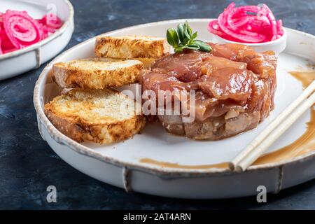 Salt marinated silver carp, diced, next to onion marinated in wine vinegar, fried croutons. Decorated with microgreen. On a wooden background. Copy sp Stock Photo