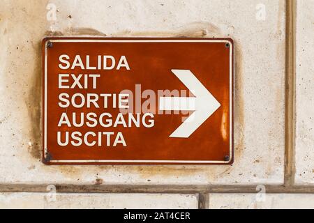 Exit in different languages, information plate with white text and arrow sign mounted on stone wall Stock Photo