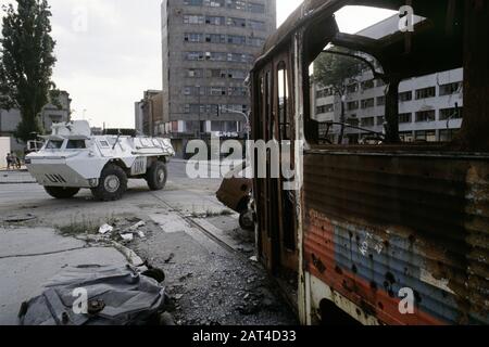 17th August 1993 During the Siege of Sarajevo: an UNPROFOR (French) Armoured Personnel Carrier turns onto Skenderija Bridge, past a burned-out tram. Stock Photo