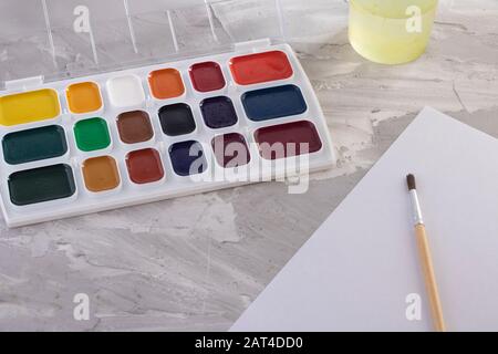 Paints, one brush and water on gray table Stock Photo