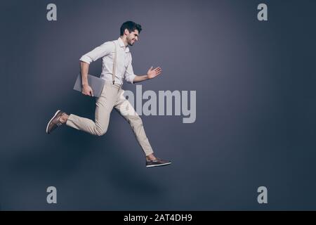 Full length profile side photo of cheerful excited guy hold computed know information about black friday discounts jump run fast wear modern clothing Stock Photo