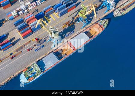 Aerial top view huge cargo ship moored at the pier at the port, loading goods, metal, concrete and other solid raw materials Stock Photo