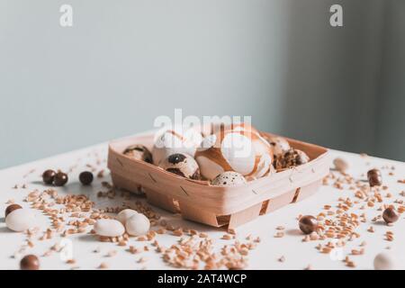 Easter day. Golden pattern Easter eggs in a wooden basket, wheat grain, chocolate candies on a white table. Congratulation Stock Photo