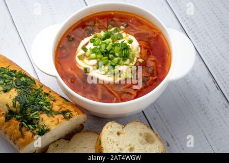 Portion of hot beetroot soup with sour cream and greens. Ukrainian traditional dish, russian cuisine. Red borscht in white bowl on wooden planks backg Stock Photo