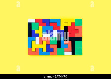 Colorful wooden blocks of different shapes puzzles on yellow background. Natural, eco-friendly toys. Creative, logical thinking concept. Background with geometric shapes wooden blocks. Stock Photo