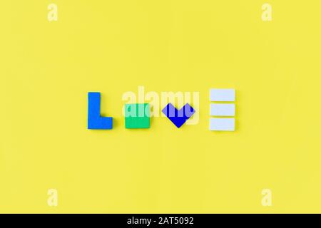Word LOVE made from colorful wooden bricks on yellow background. Parents love and kids game concept. Top view, flat lay. Stock Photo