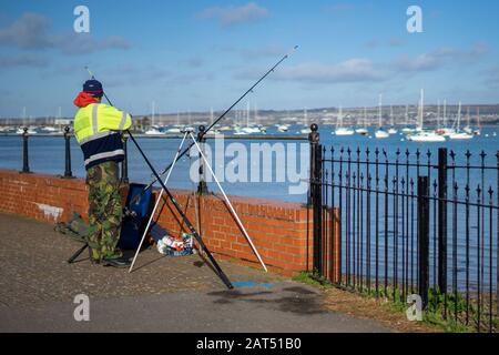 a man fishing alone at the shore with his rod on a stand Stock Photo