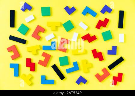 Colorful wooden blocks of different shapes puzzles on yellow background. Natural, eco-friendly toys. Creative, logical thinking concept. Background with geometric shapes wooden blocks. Stock Photo