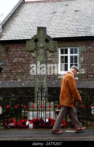 Man walking past poppy wreaths at base of war memorial in Coity village, Mid Glamorgan, Wales, UK Stock Photo