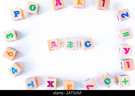 Kids toys wooden cubs with letters and numbers on white background. Frame from developing wooden blocks. Natural, eco-friendly toys for children. Top view. Flat lay. Copy space. Stock Photo