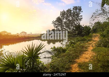 Rural India landscape with unpaved village road and pond at sunrise Stock Photo