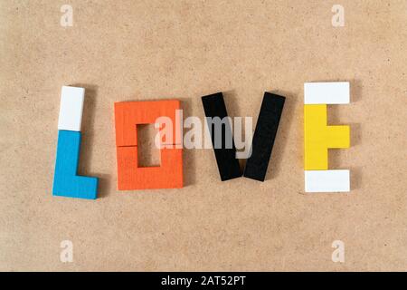 Word LOVE made from colorful wooden bricks toys on kraft cardboard background. Parents love and kids game concept. Top view, flat lay. Stock Photo