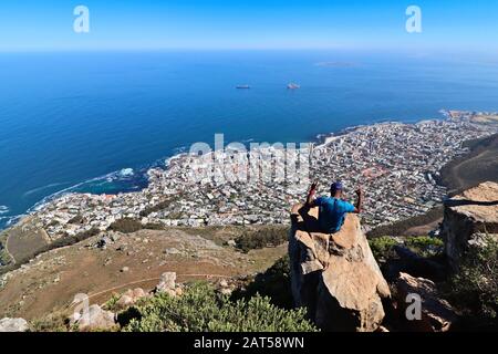 CAPE TOWN, SOUTH AFRICA - Dec 12, 2019: An African man sitting on a cliff on the top of Lion's Head mountain. This is a popular outdoor activity in th Stock Photo