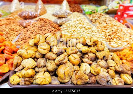 Slides with dried ugly figs, dried apricots on a background of various nuts in blurry form are sold on the shelves of the eastern market. Stock Photo