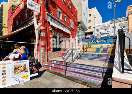 Tenerife, Spain - October 13, 2019: Colourful commercial empty street with restaurants shopping stores, ornate painted stair and steps leading up Stock Photo