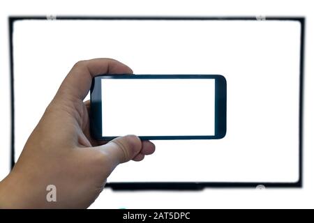 Living through the screen concept. Man holding a smartphone in front of a ultra hd tv. Both with blank screens.