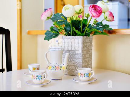 Cute teapot and cups set with floral pattern on white table beautiful persian buttercup ranunculus bunch pink white bright colors in vase no people Stock Photo