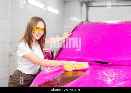 Girl washes car with yellow sponge, pink foam for cleaning Stock Photo