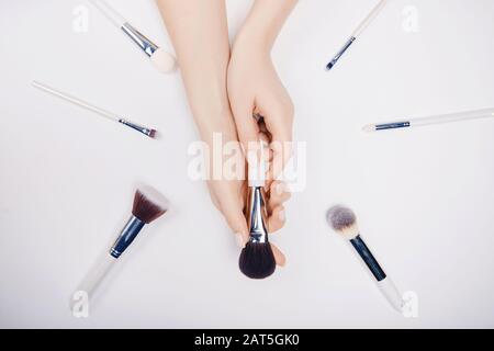 Girl hand hold white brushes makeup on white background. Top view flat lay Stock Photo