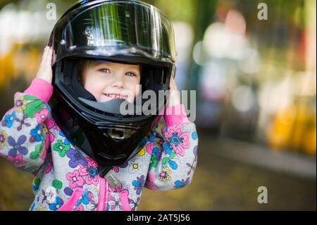 little girl in an adult motorcycle helmet smiles and holds on to a helmet. Copy space Stock Photo