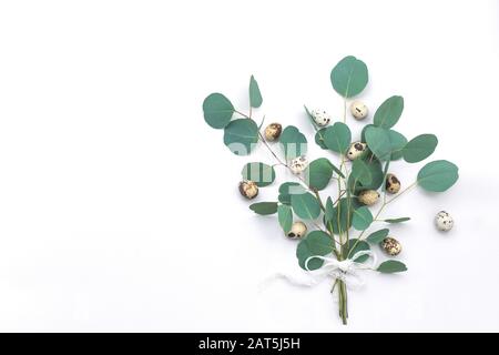 Easter bouqet composition of eucalyptus leaves and quail eggs with lace ribbon on white background. Conceptual easter bouqet greeting card. Flat lay, Stock Photo
