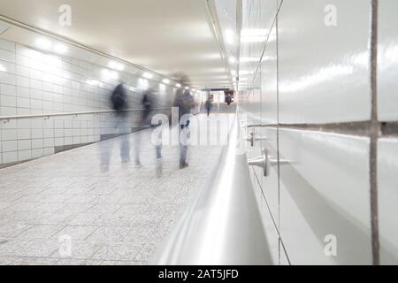 people in motion blur walking down bright white tiled tunnel walkway to subways transit Stock Photo
