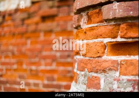 Part of an old brick post in focus and a brick wall in the background in defocus. Part of an abandoned building Stock Photo