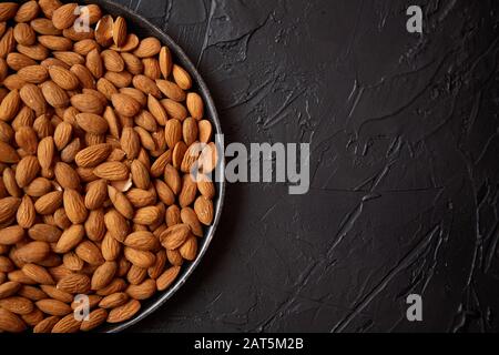 Whole almond nuts in black plate placed on black stone table Stock Photo