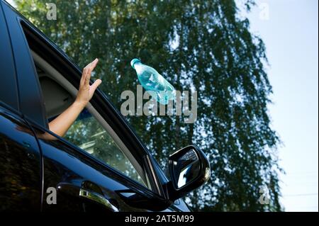 A girl throws an empty plastic bottle into the open window of a car. A flying object is slightly blurred. Bottom view, against the background of blurr Stock Photo