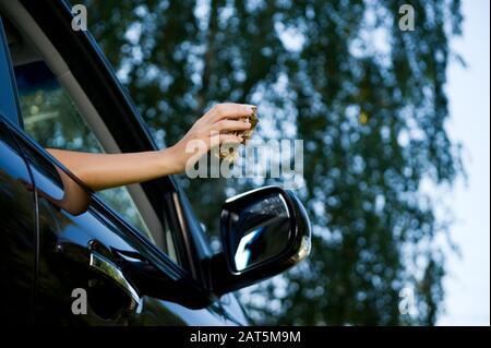 A young woman is about to throw a crumpled piece of paper or packaging from a sandwich into an open car window. View from below, on the background of Stock Photo