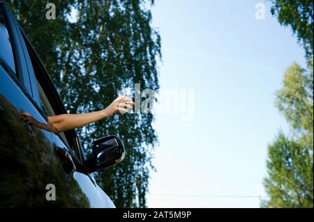 A young woman is about to throw a crumpled piece of paper or packaging from a sandwich into an open car window. View from below, on the background of Stock Photo
