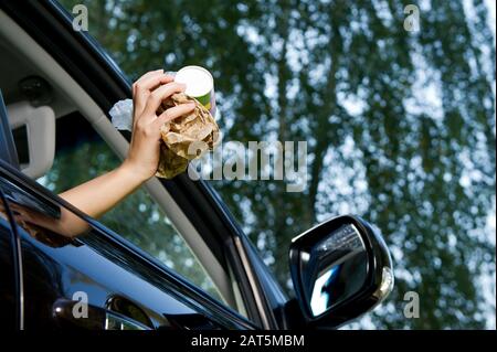 The girl is going to throw a handful of garbage accumulated in the car into the open window of the car - coffee glasses, bags, crumpled paper. Bottom Stock Photo