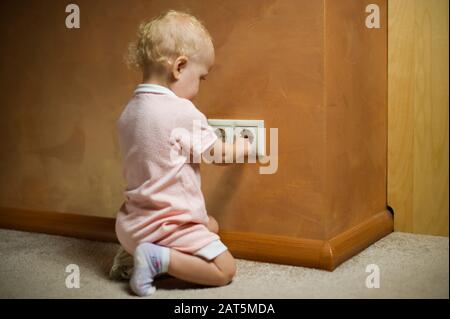 little girl is playing with an electrical outlet. A child sticks his fingers into a live outlet. Focus on an outlet Stock Photo