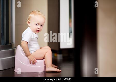 Baby girl sits on a pot in the bathroom and smiles Stock Photo