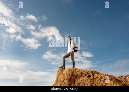 woman with backpack on the top of the rock and enjoying view, trekking, lifestyle. Stock Photo